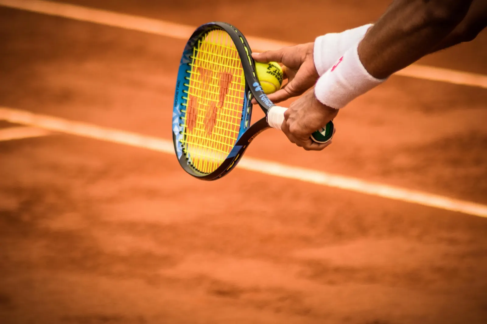 Eine Person mit Tennisschläger und Ball auf einem Sandplatz